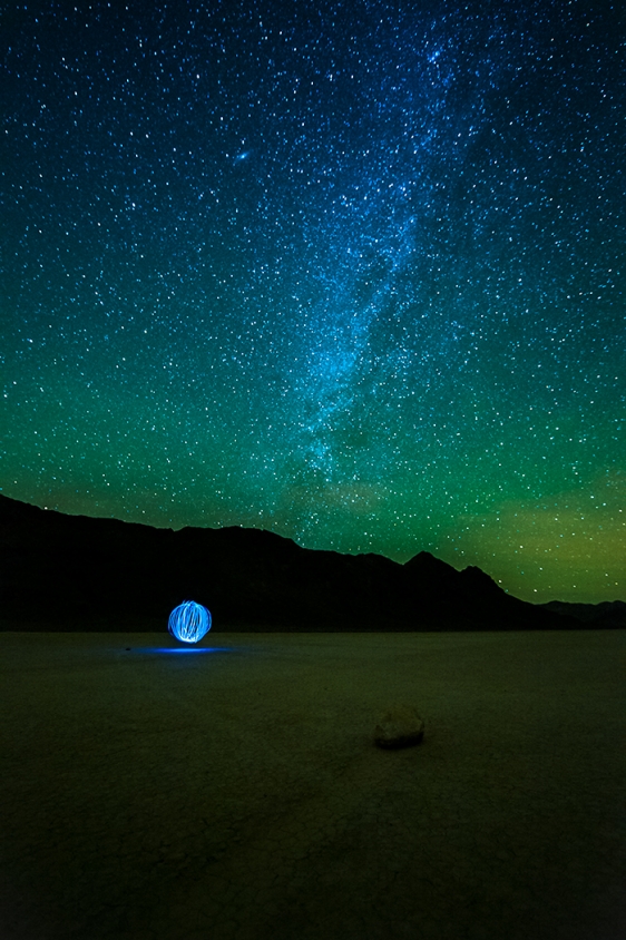Night photo Racetrack Playa dry lake bed with prominent view of milky way and a flashlight pattern that appears as an orb in the distance. Death Valley