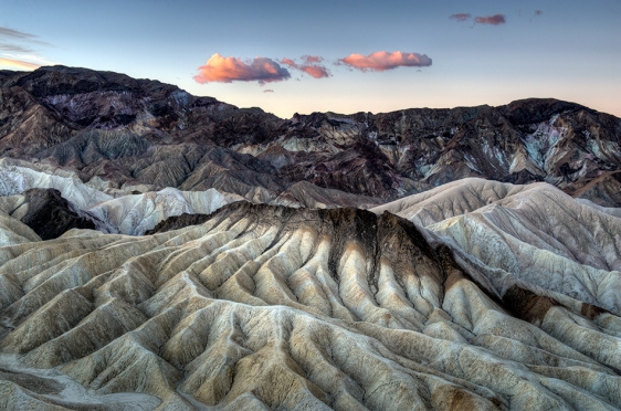 Zabriskie Point overlook in Death Valley at sunrise with trellis drainage and 2 clouds in the center.
